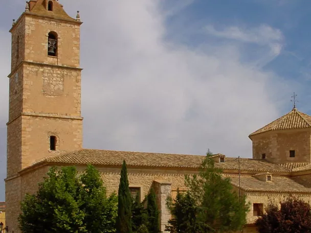 Vista exterior de iglesia de piedra con torre campanario y cúpula.