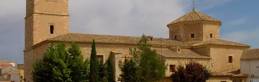 Vista exterior de iglesia de piedra con torre campanario y cúpula.