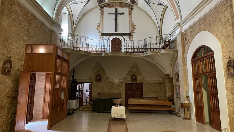 Interior del templo con coro elevado, bóveda decorada y muros de piedra.