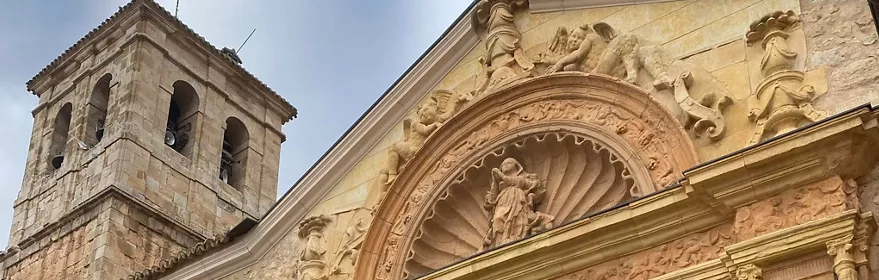 Detalle de torre campanario y frontón esculpido en fachada de piedra.