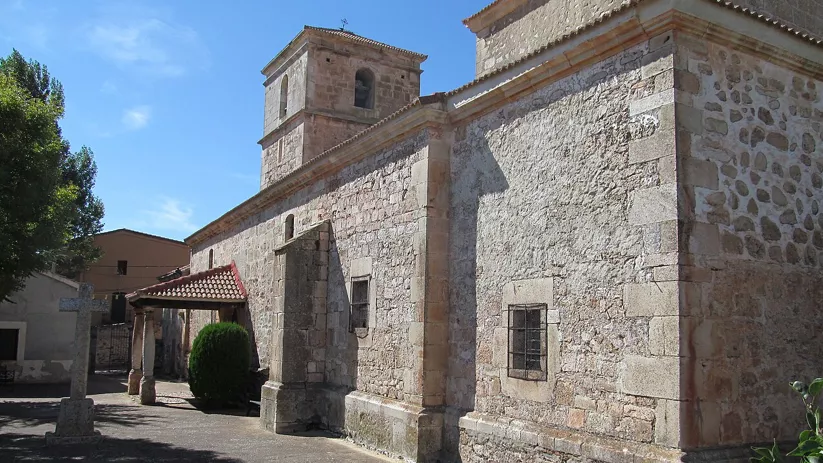 Iglesia de piedra vista desde un lateral, con torre y pequeño atrio porticado.