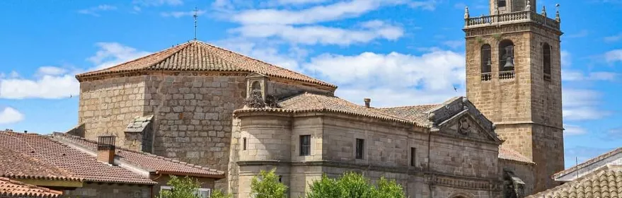 Vista exterior de un templo de piedra con torre campanario bajo un cielo azul.