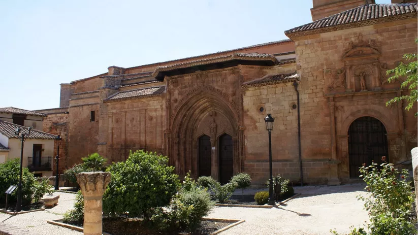 Fachada de templo de piedra con portada gótica y jardín delantero.