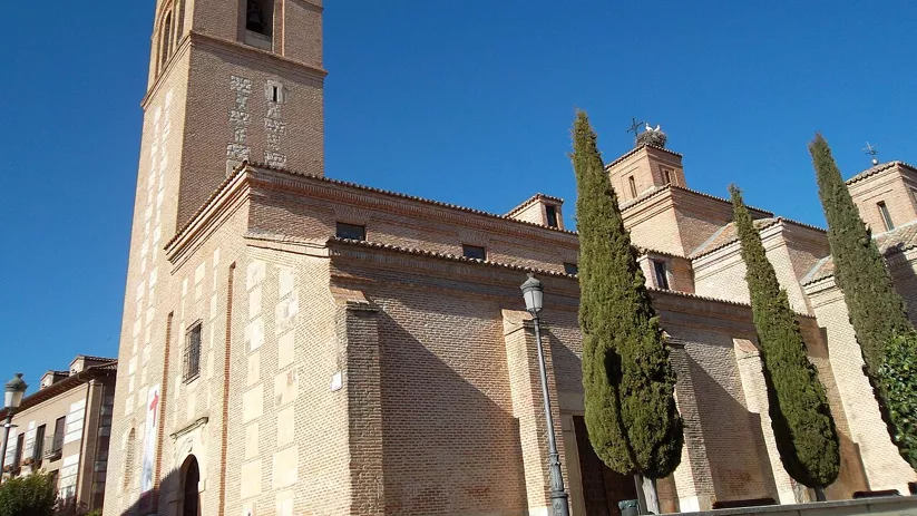 Iglesia de ladrillo con torre campanario y cipreses bajo cielo despejado.