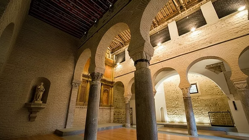 Interior con arcos de herradura y columnas de piedra sobre suelo de madera.