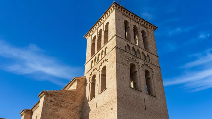 Torre campanario de ladrillo bajo cielo azul intenso.