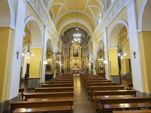 Interior de iglesia con bóveda amarilla, bancos de madera y retablo dorado.