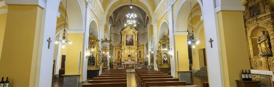 Interior de iglesia con bóveda amarilla, bancos de madera y retablo dorado.