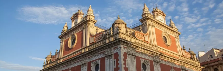 Fachada barroca en tonos rojizos con torres y cúpulas bajo cielo azul.