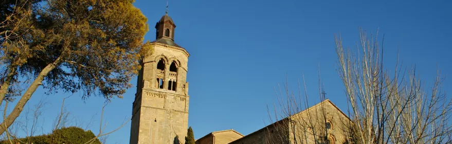 Iglesia de piedra en lo alto con torre y árboles sin hojas al atardecer.