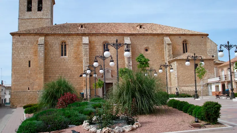 Iglesia de piedra con torre y jardines en una plaza.