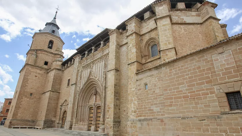 Fachada lateral de una iglesia de piedra con torre campanario y portada monumental.