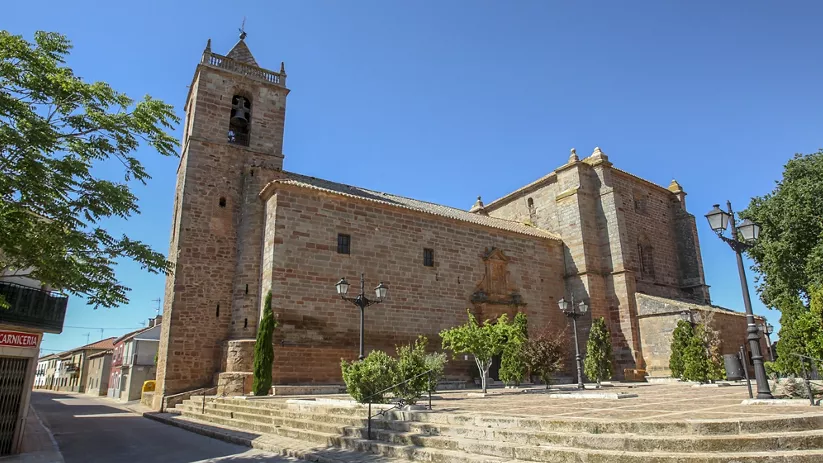 Iglesia de piedra con torre campanario y escalinata en una plaza.