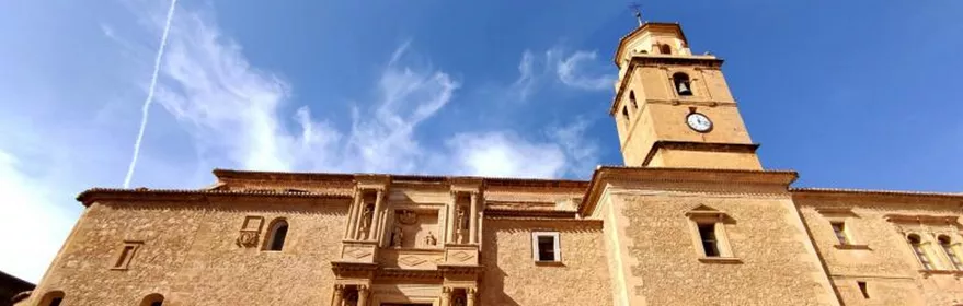 Iglesia vista desde abajo, con escalinata de acceso, portada central y torre con reloj.