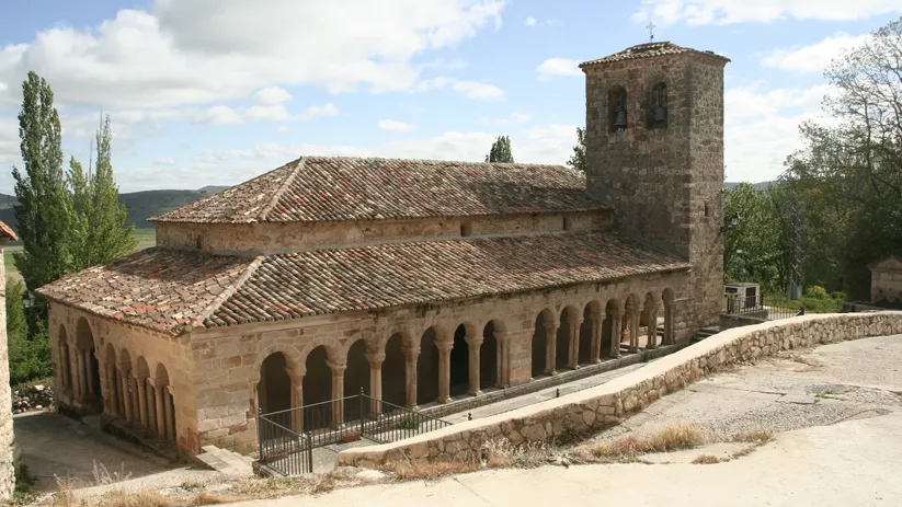 Iglesia de piedra con torre campanario y pórtico lateral.