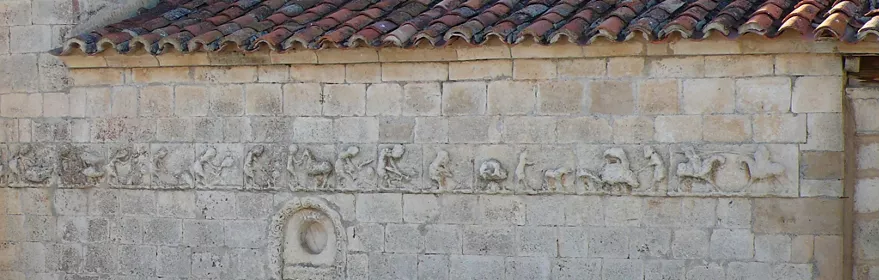 Friso escultórico románico en muro de iglesia de piedra.