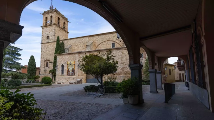 Plaza porticada con edificio de piedra y torre campanario