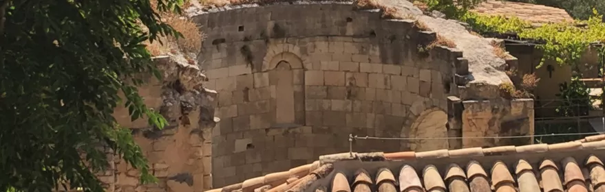 Ábside de piedra entre tejados y árboles.