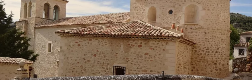Iglesia de piedra con torre campanario y tejado de teja curva.