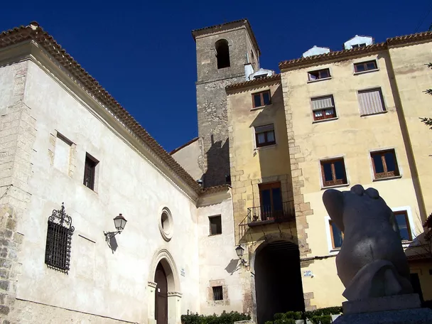 Fachada de iglesia con torre de piedra y escultura en plaza histórica.