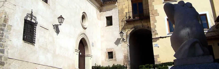 Fachada de iglesia con torre de piedra y escultura en plaza histórica.