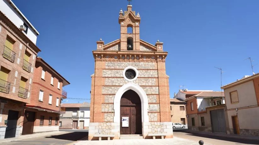 Fachada de iglesia de ladrillo y piedra con arco apuntado y espadaña, en plaza urbana.