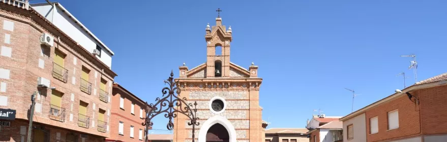 Plaza abierta con pozo central y pequeña iglesia al fondo entre edificios residenciales.