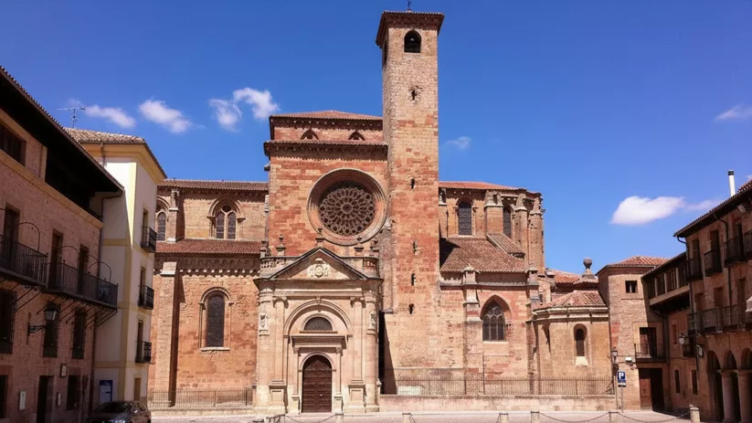 Fachada de piedra con rosetón y torre sobre plaza empedrada.