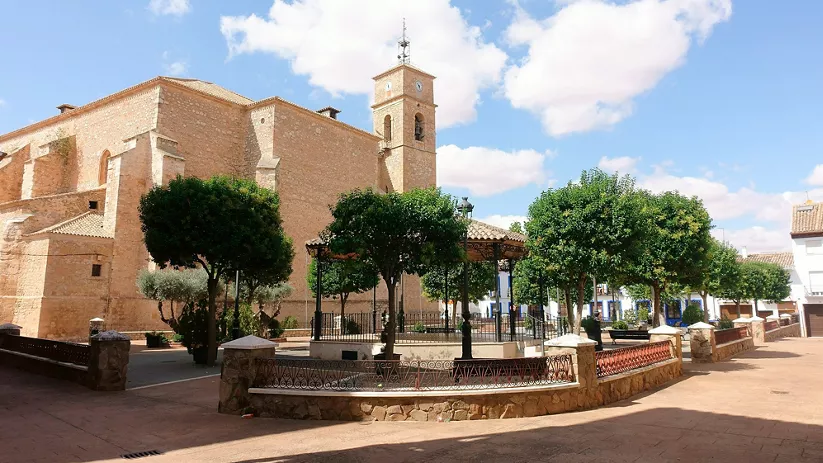 Plaza arbolada con iglesia de piedra y quiosco central