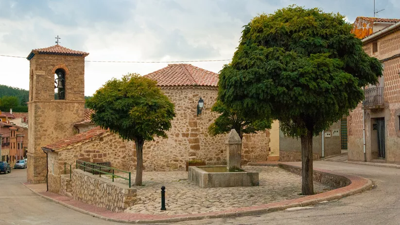 Plaza empedrada con iglesia de piedra y árboles.