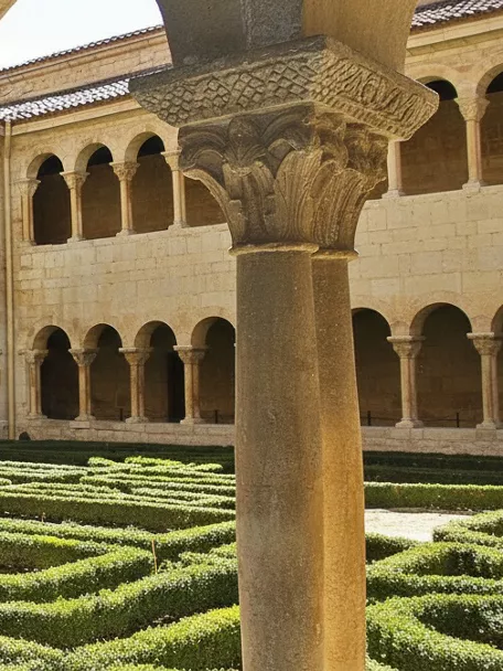 Claustro románico con arcos y jardín geométrico.