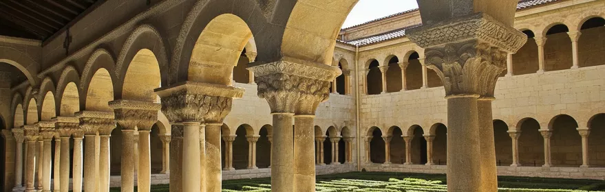 Claustro románico con arcos y jardín geométrico.