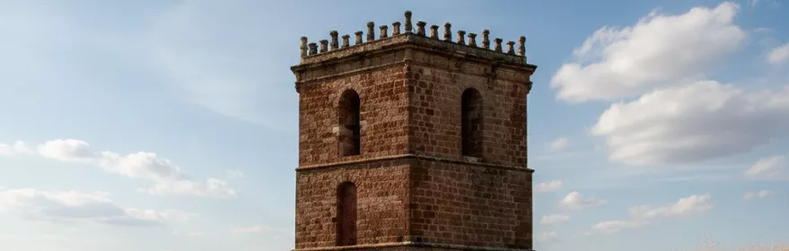 Torre de piedra aislada sobre colina cubierta de hierba seca.