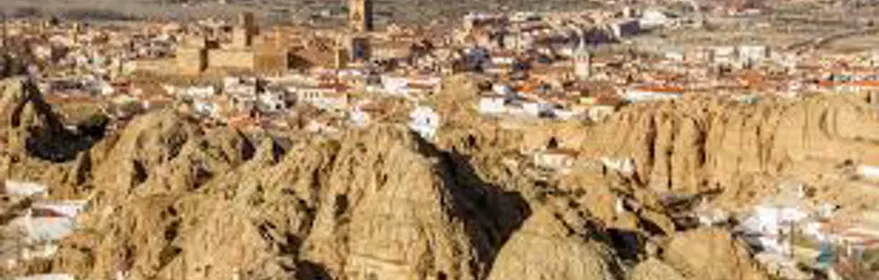 Vista panorámica de ciudad con casas bajas y formaciones rocosas en primer plano.