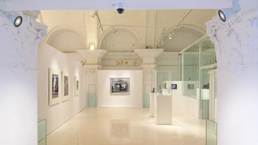 Interior de museo con columnas decoradas y obras en pared.