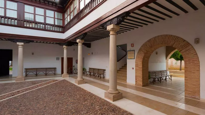 Patio interior de palacio histórico con columnas de piedra, galerías de madera y suelo empedrado tradicional.