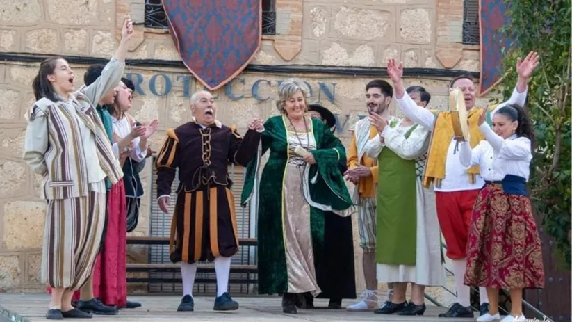 Grupo de actores con vestuario histórico saludando al público sobre un escenario al aire libre.