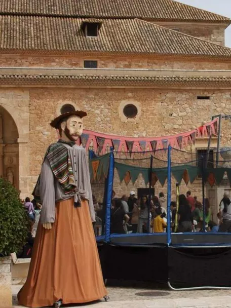 Plaza decorada para una feria con atracciones, puestos y una figura gigante tradicional.