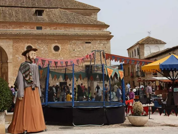 Plaza decorada para una feria con atracciones, puestos y una figura gigante tradicional.
