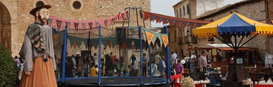 Plaza decorada para una feria con atracciones, puestos y una figura gigante tradicional.