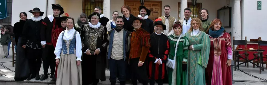Grupo de personas con vestimenta histórica posando delante de un edificio con balcones.