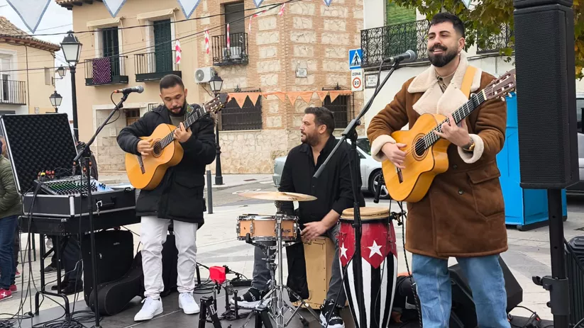 Tres músicos actúan en la calle con guitarras, micrófonos y percusión.