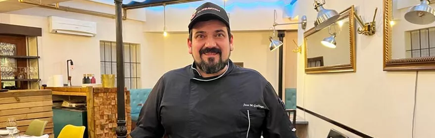 Cocinero con chaqueta negra posa en el comedor de un restaurante