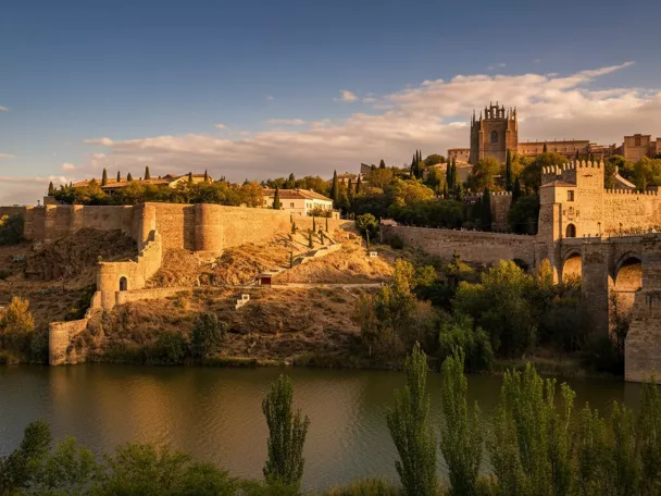 Vista panorámica de murallas, puente y río al atardecer.