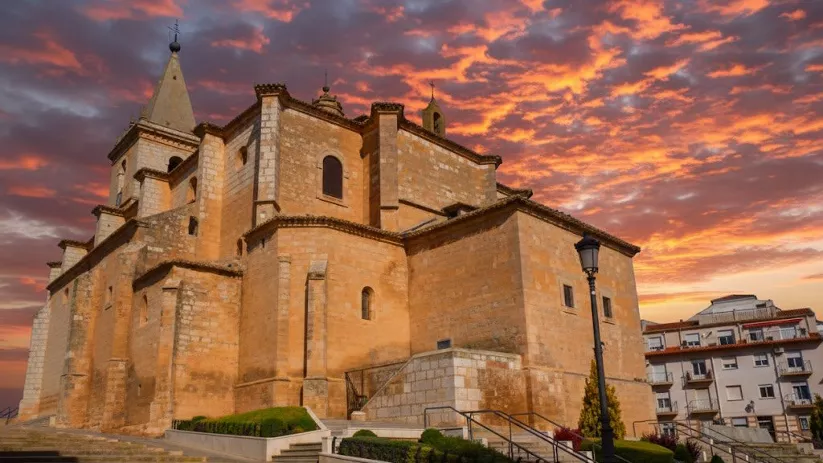 Iglesia de La Gineta sobre una plaza elevada, con cielo rojizo al atardecer.