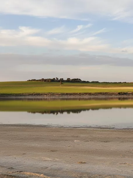 Reflejo de una laguna tranquila frente a campos y lomas