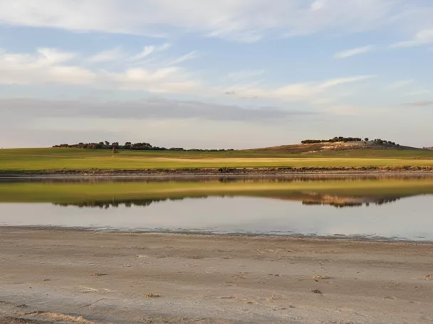 Reflejo de una laguna tranquila frente a campos y lomas
