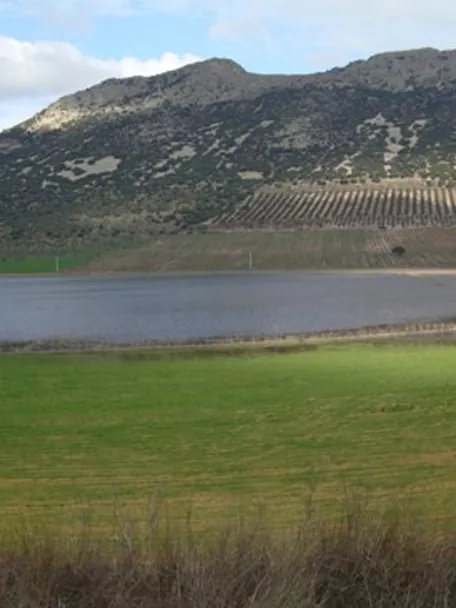 Panorámica de laguna rodeada de campos verdes y sierras suaves