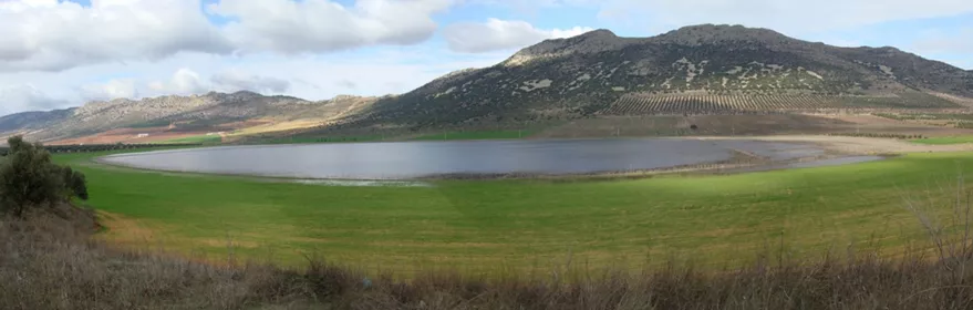 Panorámica de laguna rodeada de campos verdes y sierras suaves