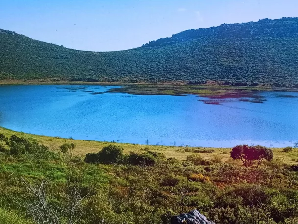 Laguna rodeada de matorral y colinas bajo cielo azul